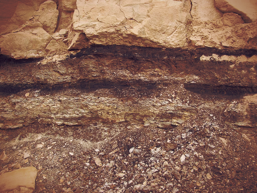 ユタ州にある地層がむき出しになった赤茶けた壮大な大地。中でも黒っぽい一層が、大恐竜時代の白亜紀の地層。